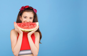Pretty girl holding slice of watermelon in front of her face. Portrait of smiling teen girl isolated on blue background.