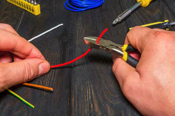 The master holds a power tool and cuts the red wire to connect