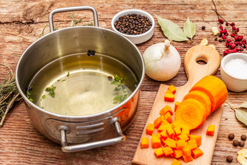 Transparent duck broth in pan with fresh ingredients. Traditional bouillon for healthy dishes. Spices, vegetables, old wooden table