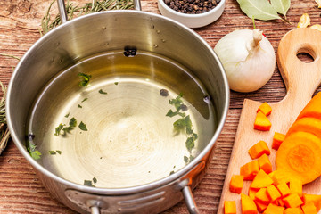 Transparent duck broth in pan with fresh ingredients. Traditional bouillon for healthy dishes. Spices, vegetables, old wooden table