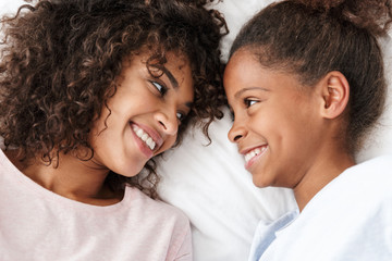 Image of cheerful african american woman and her daughter lying in bed