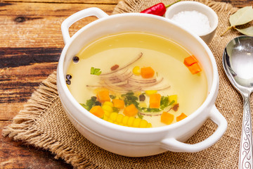 Transparent duck broth in bowl with vegetables. Traditional bouillon, healthy meal. Old wooden background