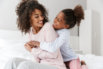 Image of african american woman and her little daughter hugging in bedroom