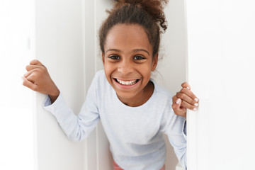 Image of african american little girl playing hide and seek in closet