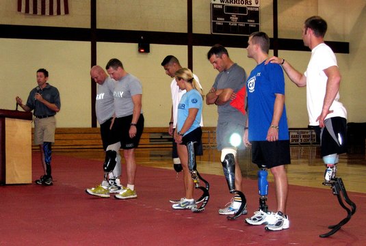 Brian Frasure paralympian speaking at a Military Amputees Training workshop while flanked by seven soldiers wearing advanced artificial legs