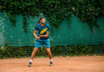 Concentrated man playing tennis, holding a racket and watching the bal