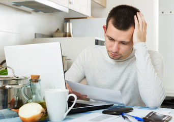 Male freelancer reading papers near laptop