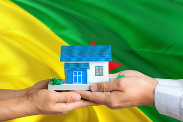 French Guiana real estate concept. Man and woman holding miniature house in hands. Citizenship theme and national flag on background.