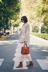 fashion blogger street style. fashionable woman posing wearing an oversized blazer, floral vintage dress, suede cowboy ankle boots and a black trendy mini handbag. perfect fall 2019 outfit.  © mlasaimages