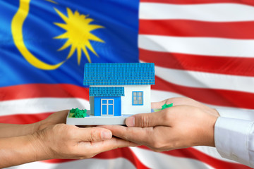 Malaysia real estate concept. Man and woman holding miniature house in hands. Citizenship theme and national flag on background.