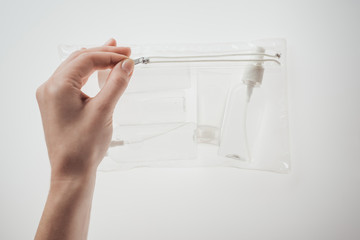 cropped view of woman holding cosmetic bag with bottles and tube on white background