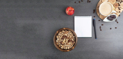 banner of Coffee break in the workplace. White cup of coffee, apple, mix of nuts in wooden bowl, notepad, pen on grey background, top view