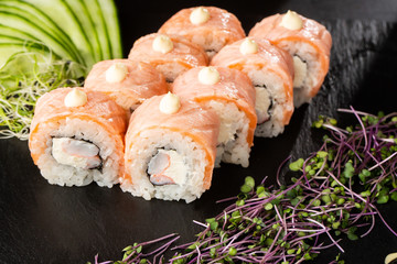 Sushi Rolls with flamed salmon, shrimp, crab meat and Cream Cheese inside on black slate isolated. Philadelphia roll sushi with shrimp. Sushi menu. Horizontal photo.
