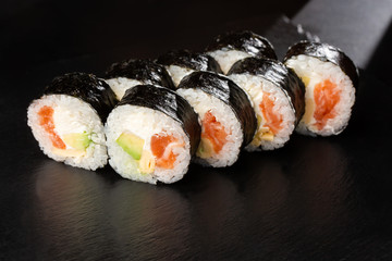 Sushi Rolls with salmon, avocado, omelet and Cream Cheese inside. Maki Futomaki Sushi Rolls with salmon on black background. Sushi menu. Japanese food. Horizontal photo.