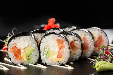 Sushi Rolls with salmon, avocado, omelet and Cream Cheese inside. Maki Futomaki Sushi Rolls with salmon on black background. Sushi menu. Japanese food. Horizontal photo.