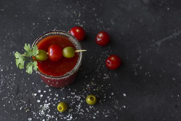 Spicy Vodka Bloody Mary cocktails served with pickled veggies (tomatos, olive and celery) on a dark background.