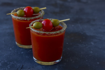 Spicy Vodka Bloody Mary cocktails served with pickled veggies (tomatos, olive and celery) on a dark background.
