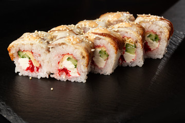 Sushi Rolls with cucumber, flying fish caviar, eel, omelet and Cream Cheese inside on black slate isolated. Philadelphia unagi roll sushi with tamago. Sushi menu. Horizontal photo.