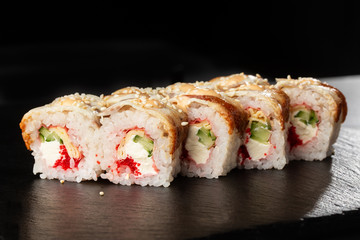 Sushi Rolls with cucumber, flying fish caviar, eel, omelet and Cream Cheese inside on black slate isolated. Philadelphia unagi roll sushi with tamago. Sushi menu. Horizontal photo.