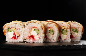 Sushi Rolls with cucumber, flying fish caviar, eel, omelet and Cream Cheese inside on black slate isolated. Philadelphia unagi roll sushi with tamago. Sushi menu. Horizontal photo.