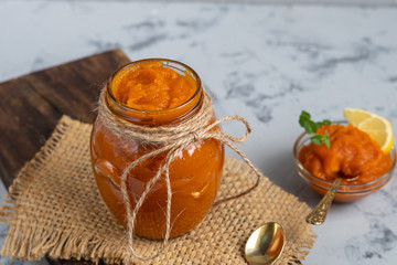 Carrot jam with orange juice, decorated with mint and slices of lemon on a pineapple, stone background. Autumn product. The horizontal location. Copy space. Flat lay. 