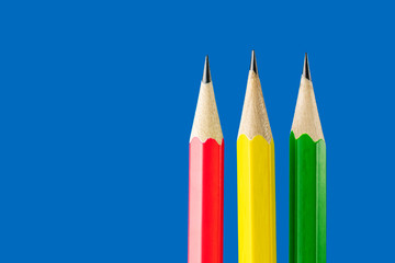 Yellow, green and red pencils close-up on a blue background. The concept of materials for drawing, training, art therapy. Minimalism, place for text.
