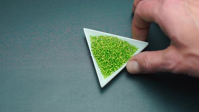 Close-up of a hand twirls a triangular plate with green beads.