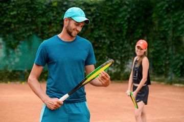 Man looking at his racket, while woman smiling in the background.