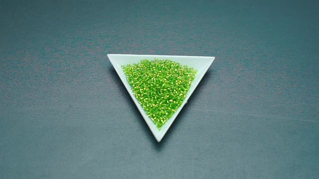 The jeweler takes a triangular plate with beads with his hand.