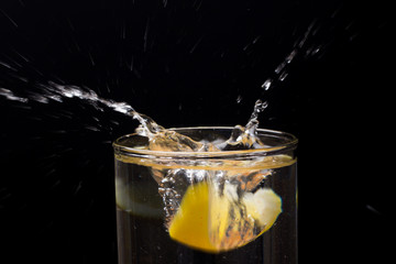 Limón entrando en un vaso o jarro de cristal transparente lleno de agua, chapoteo, agua salpicando...