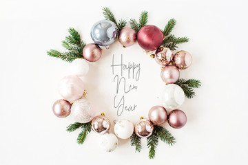 Christmas / New Year holiday composition. Quote "Happy New Year" in frame wreath with Christmas baubles, balls and fir branches on white background. Flat lay, top view festive concept.