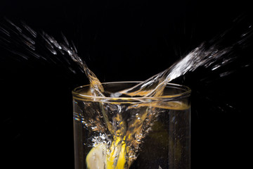 Limón entrando en un vaso o jarro de cristal transparente lleno de agua, chapoteo, agua salpicando y saliendo del vaso