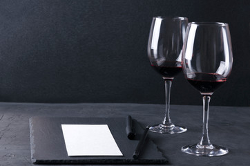 Process of wine tasting. Wineglasses, paper, pen on the dark table against black background