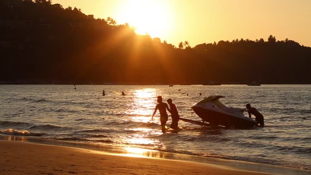 Men at sunset pull hydro cycle out of the water on a sandy beach.  Summer vacation. Water bike loading in to  trailer