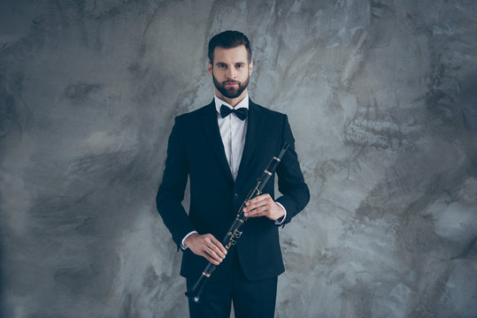 Photo of serious porfessional musician readying to play clarinet with beard on face isolated grey color concrete wall background