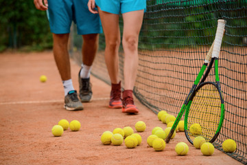 Plenty of balls laying on a outdoor court and two rackets.
