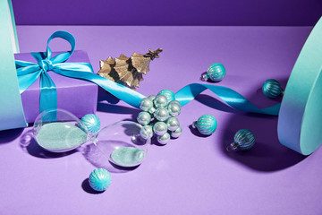 Christmas decoration and hourglass scattered from blue gift box on purple background