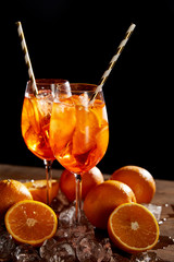 Aperol Spritz in glasses, oranges and ice cubes on black background