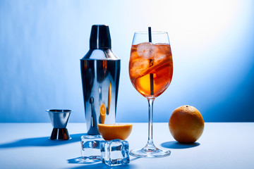 cocktail Aperol Spritz, oranges, shaker, ice cubes and measuring cup on blue background