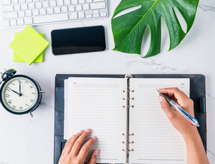 Hand of woman writing on notebook with office accessories Top view on Modern table.Business...