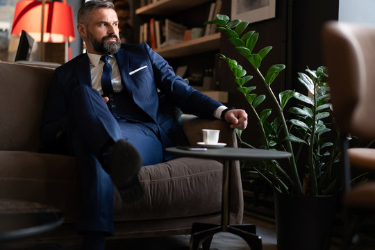 Starting New Working Day. Handsome Man Holding Coffee Cup Sitting On The Couch In Office.