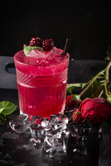 Alcoholic cocktail with blackberries, mint and ice on a dark wooden background. Refreshing red drink in a glass