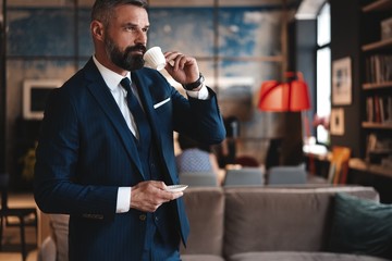 Confident man in smart casual wear holding coffee cup at his working place in office