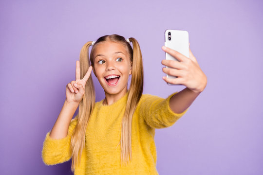 Portrait of funny funky child piggytails ponytails enjoy trip take selfie make v-signs wear stylish yellow pullover isolated over purple color background