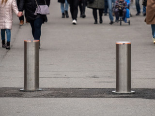 Automatic cylindrical barriers on the pedestrian zone against the background of blurry feet of pedestrians.