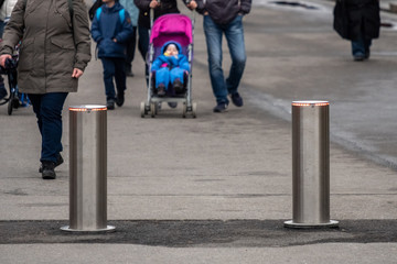 Automatic cylindrical barriers on the pedestrian zone against the background of blurry feet of pedestrians.
