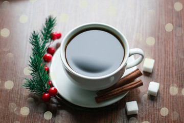 A white cup of coffee with sprig of christmas tree, cinnamon sticks and sugar cubes