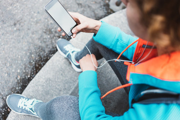 Sporty young woman holding mobile phone in hands, while resting on the stairs. Close-up