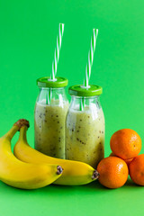 banana and kiwi smoothie with tangerines on a green background