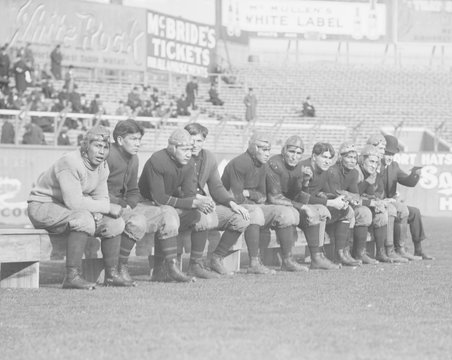 Carlisle Indian School, football players on the bench, during a game at the Polo Grounds, NYC, 1909